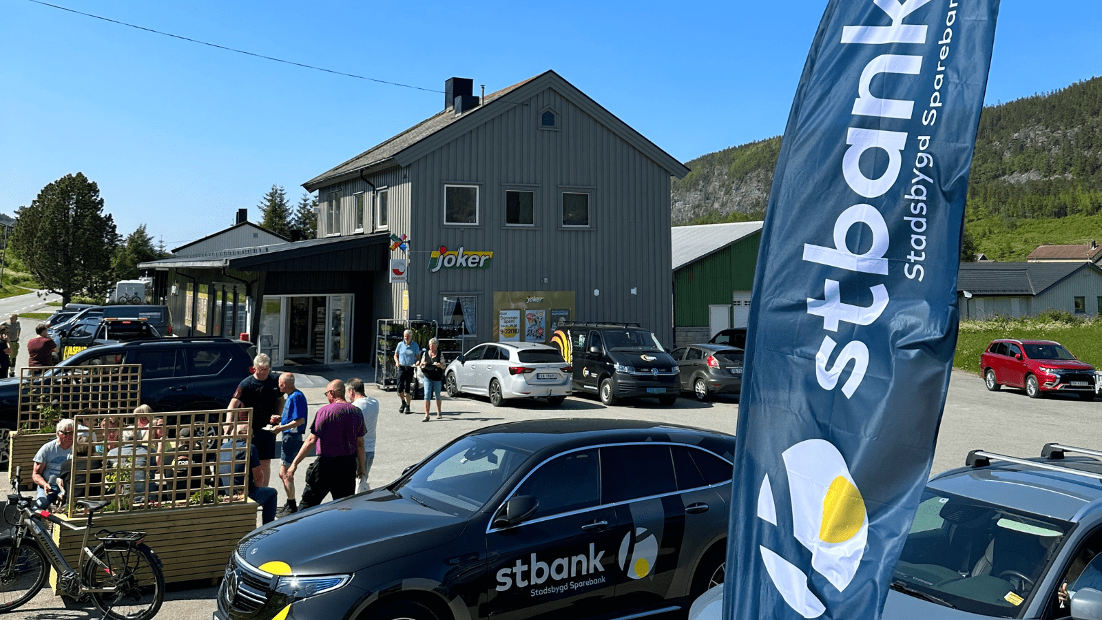 Bilde av Stbank bil og flagg med joker Husbysjøen i bakgrunn