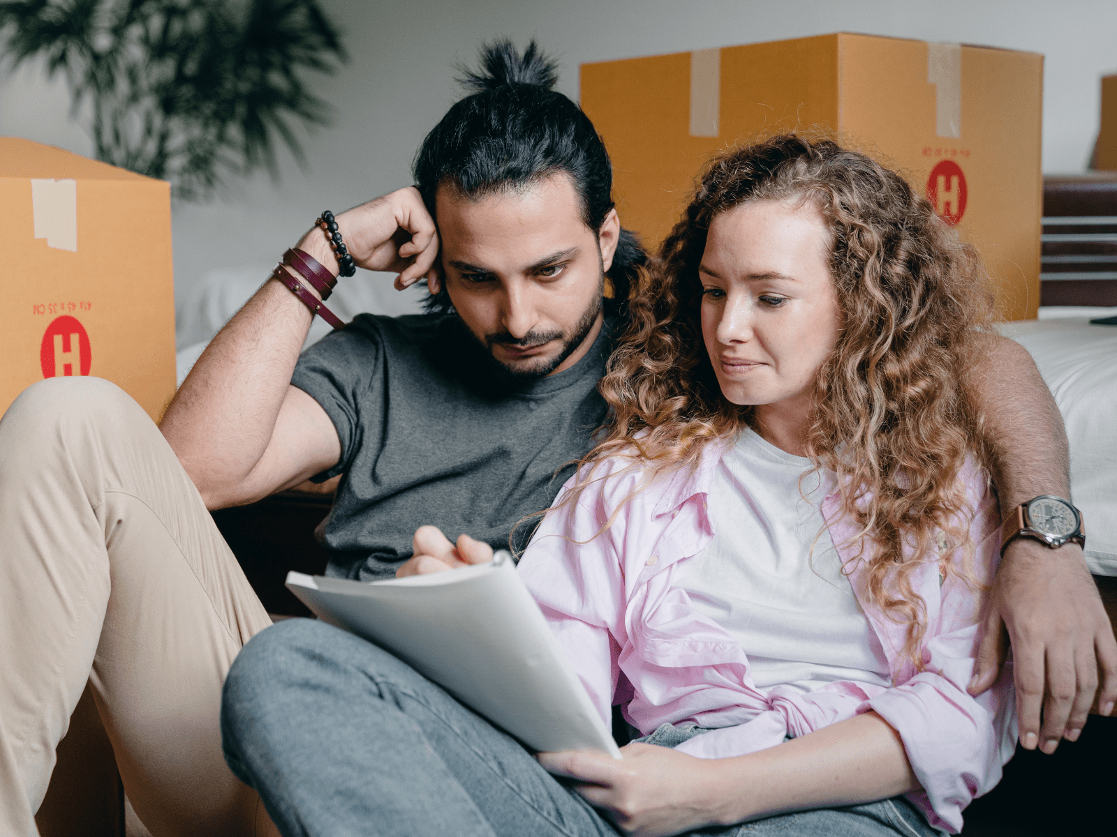 Et par som sitter i en sofa og ser på et ark med flytteesker i bakgrunnen 